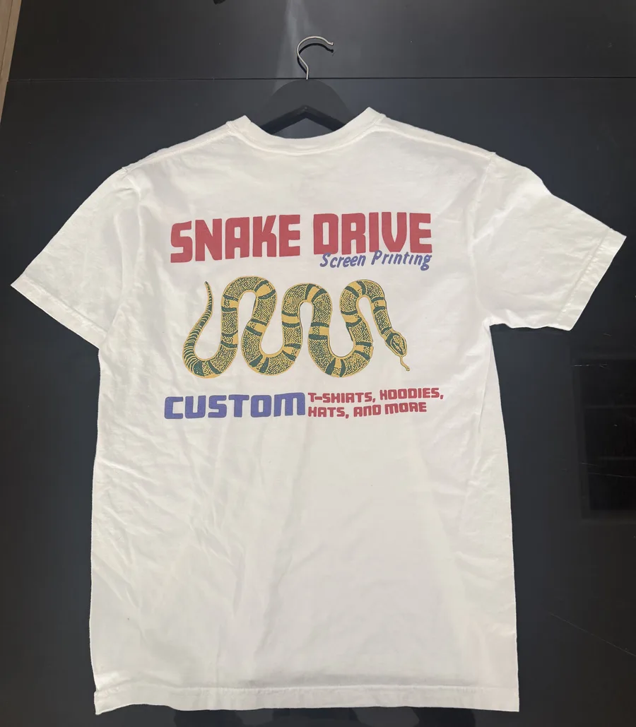 A white tee laid flat with a red, blue, yellow and green Snake Drive Screen Printing back print of a snake